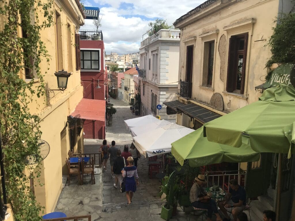 a group of people walking down a narrow street with tables and umbrellas