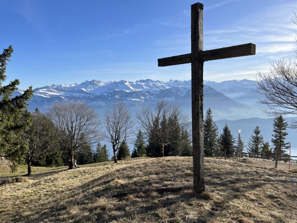 a cross on a hill with trees and mountains in the background