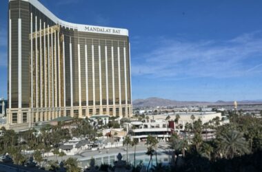 a large building with a pool and palm trees with Mandalay Bay in the background