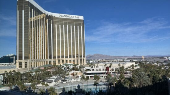 a large building with a pool and palm trees with Mandalay Bay in the background