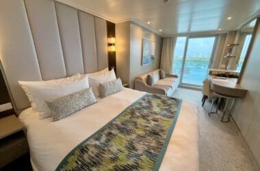 a bed in a room with a balcony and a table on the Sun Princess Deluxe Balcony