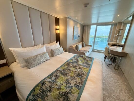 a bed in a room with a balcony and a table on the Sun Princess Deluxe Balcony