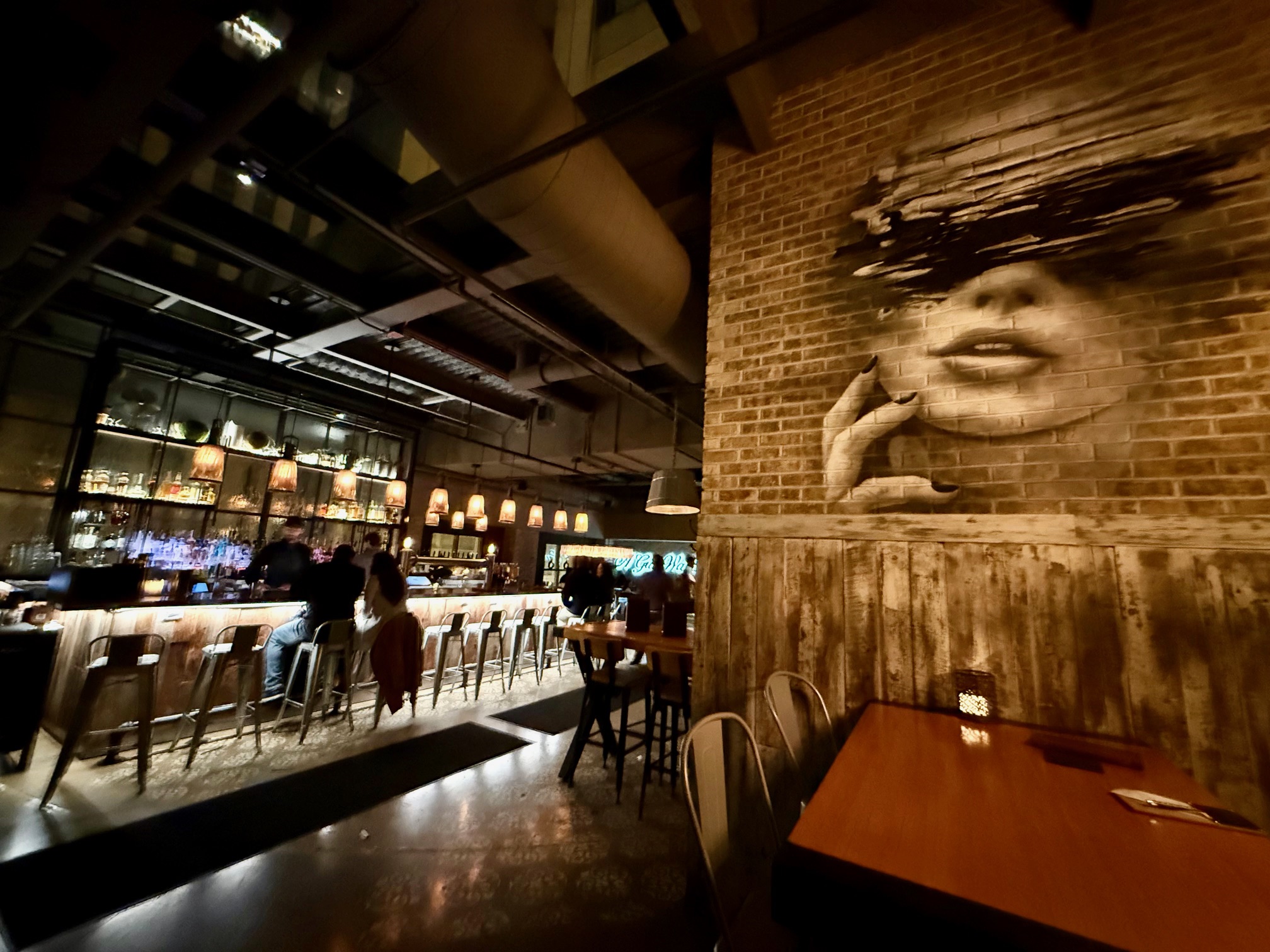 a room with a brick wall and a bar with people sitting at tables