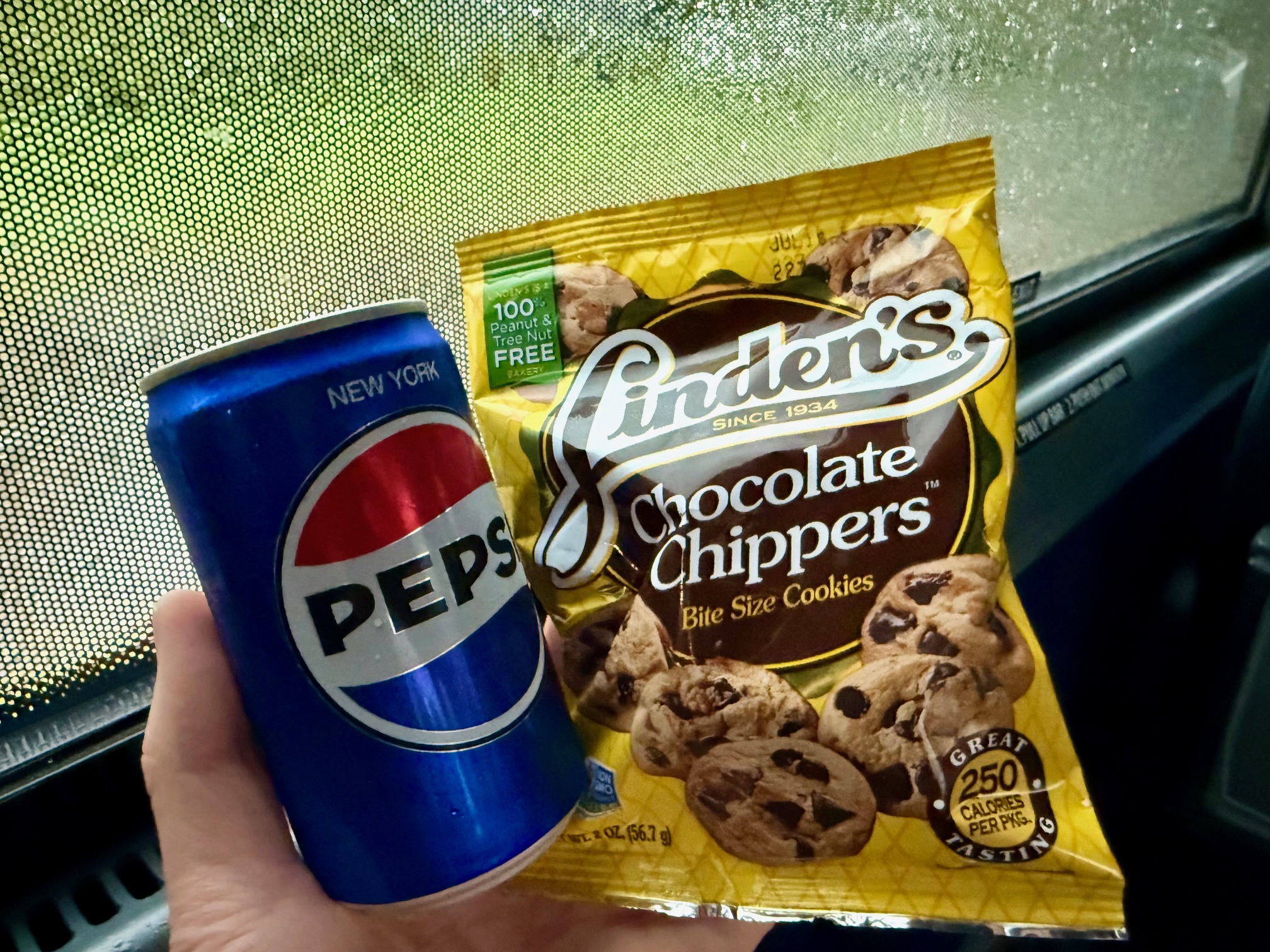 a hand holding a can of soda and a bag of cookies