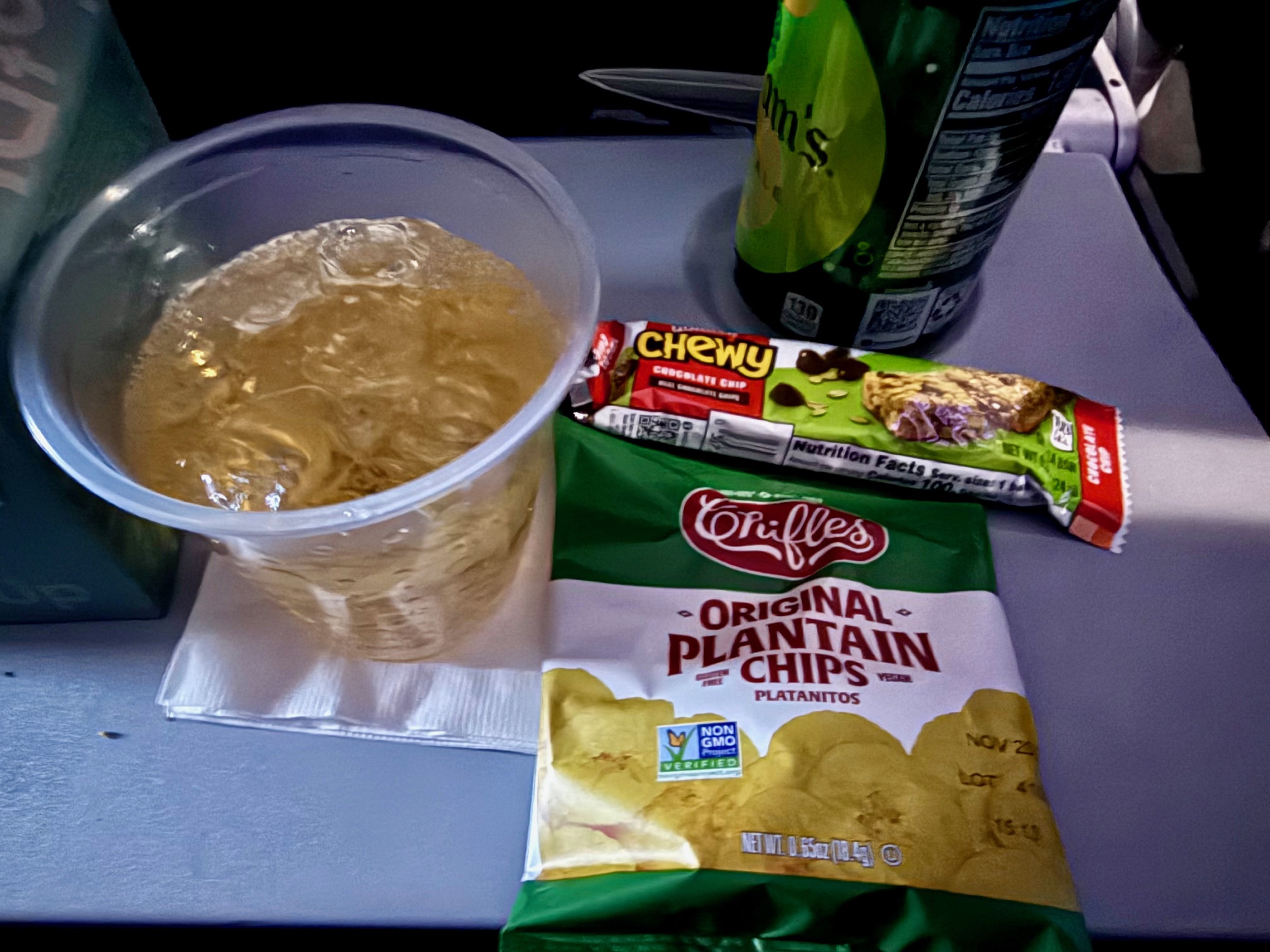 a plastic cup of liquid next to a bag of chips and a can of chips