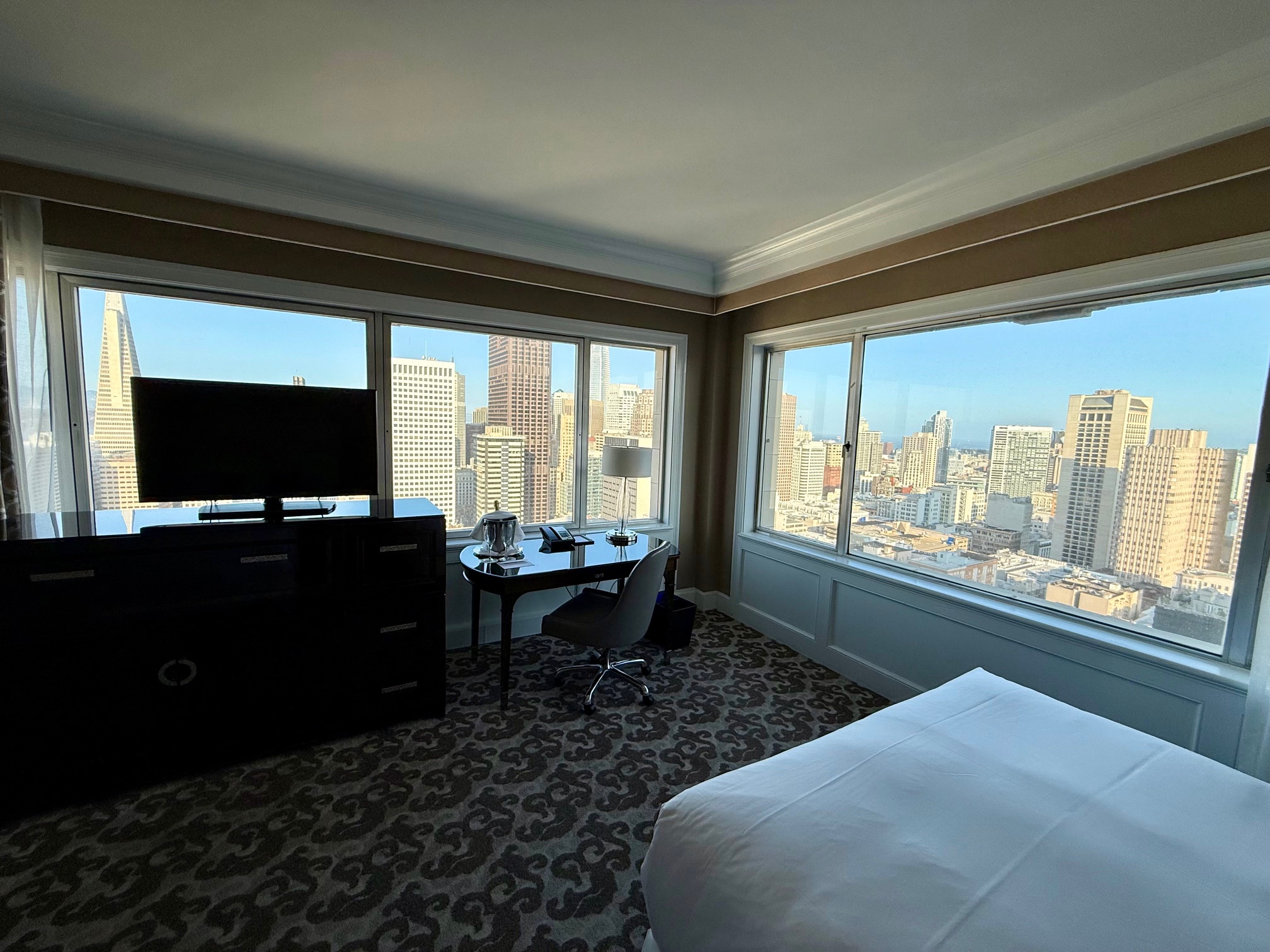 a room with a bed and a desk and a window with a city view