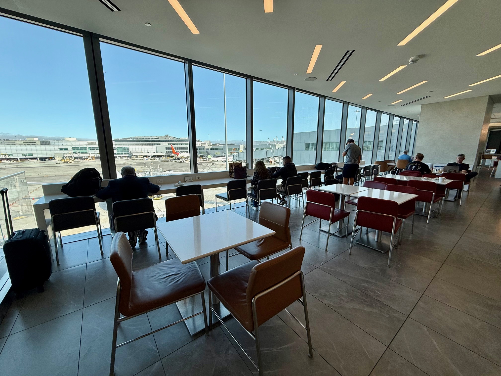 a group of people sitting at tables in a room with large windows at the Admirals Club San Francisco
