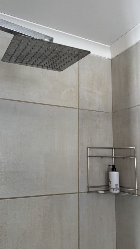 a shower head with a white tile wall and a white shelf with a white bottle of soap