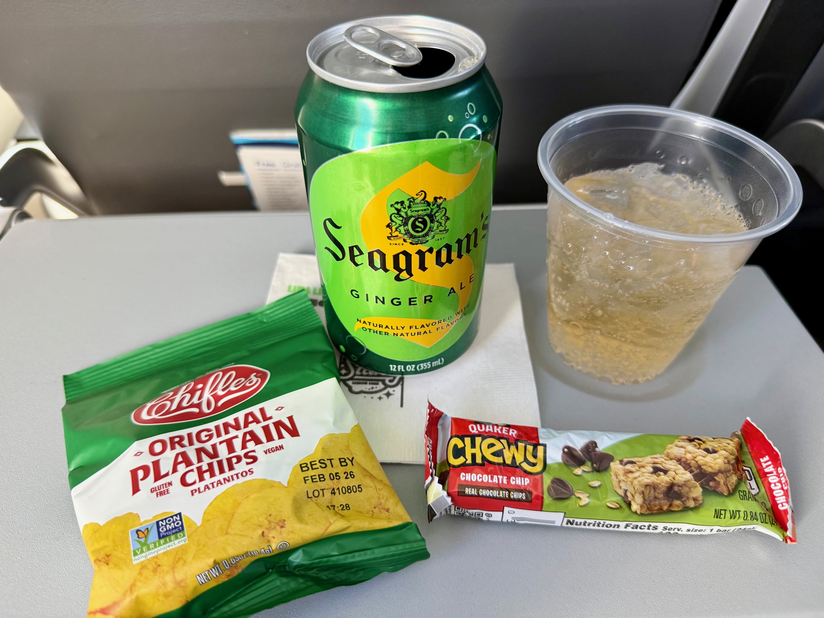 a can of soda and a cup of soda next to a bag of chips on the JetBlue Airbus A220