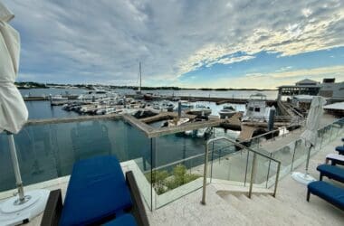 a deck with chairs and a glass railing next to a body of water