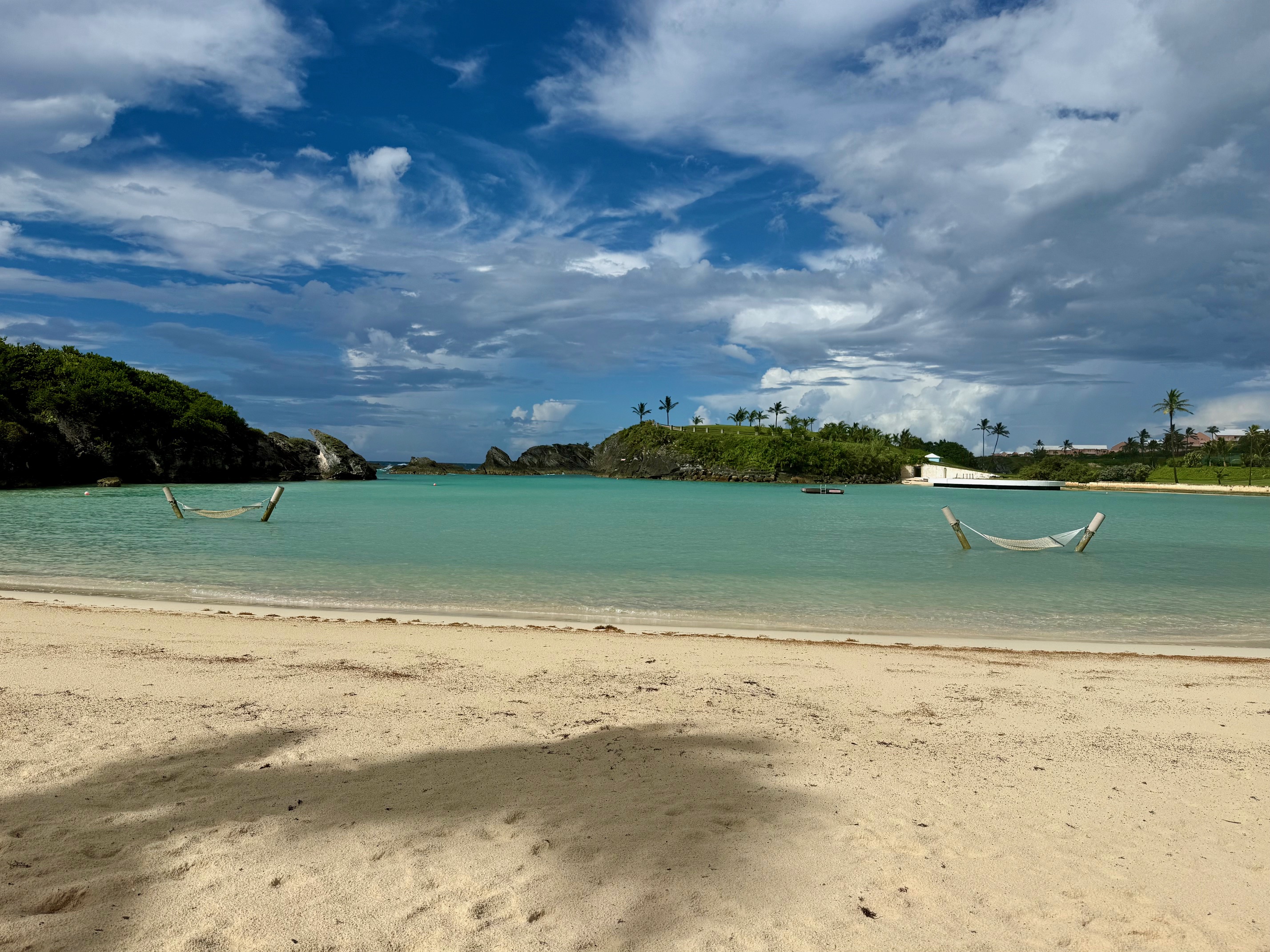 hammocks in the water on a beach with trees and blue sky at the Fairmont Hamilton Princess Beach Club
