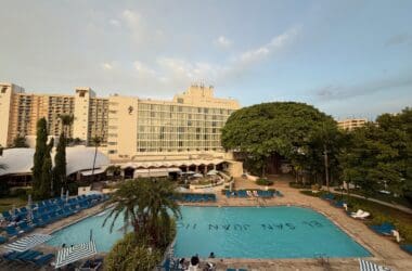 a pool with chairs and trees in front of a building