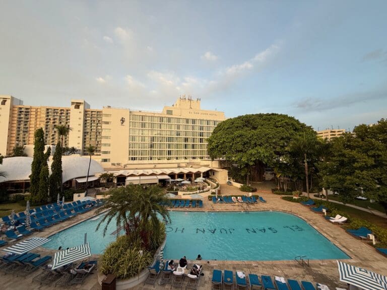 a pool with chairs and trees in front of a building