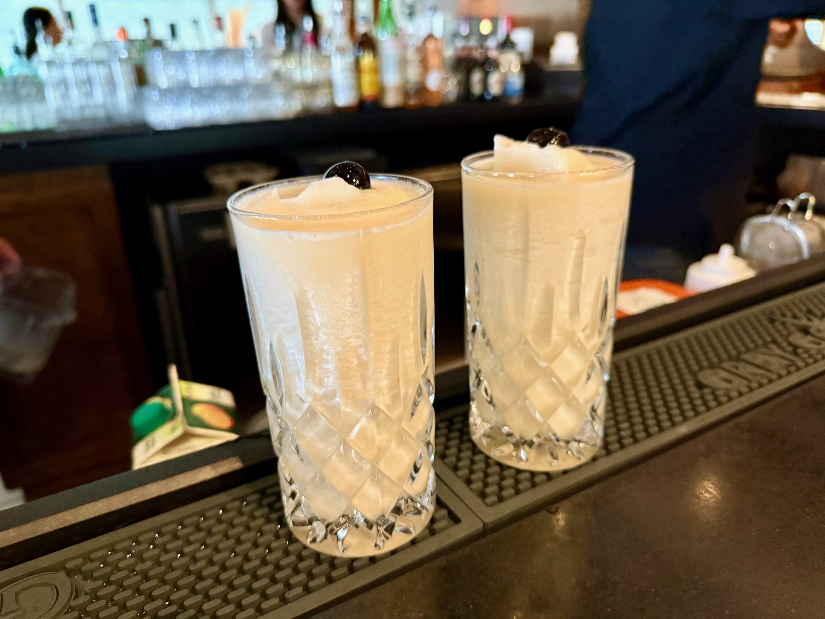 two glasses of white liquid on a bar
