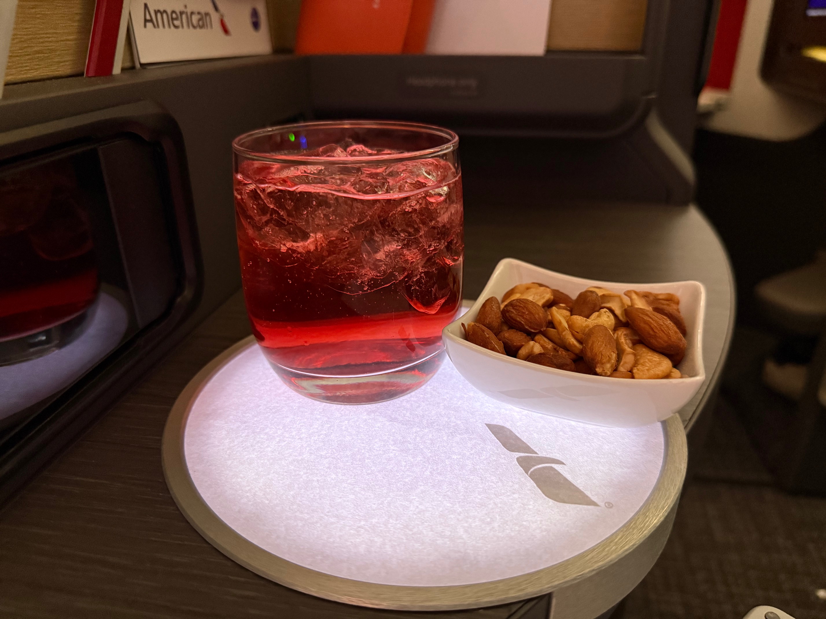 a glass of red liquid and a bowl of nuts on a tray