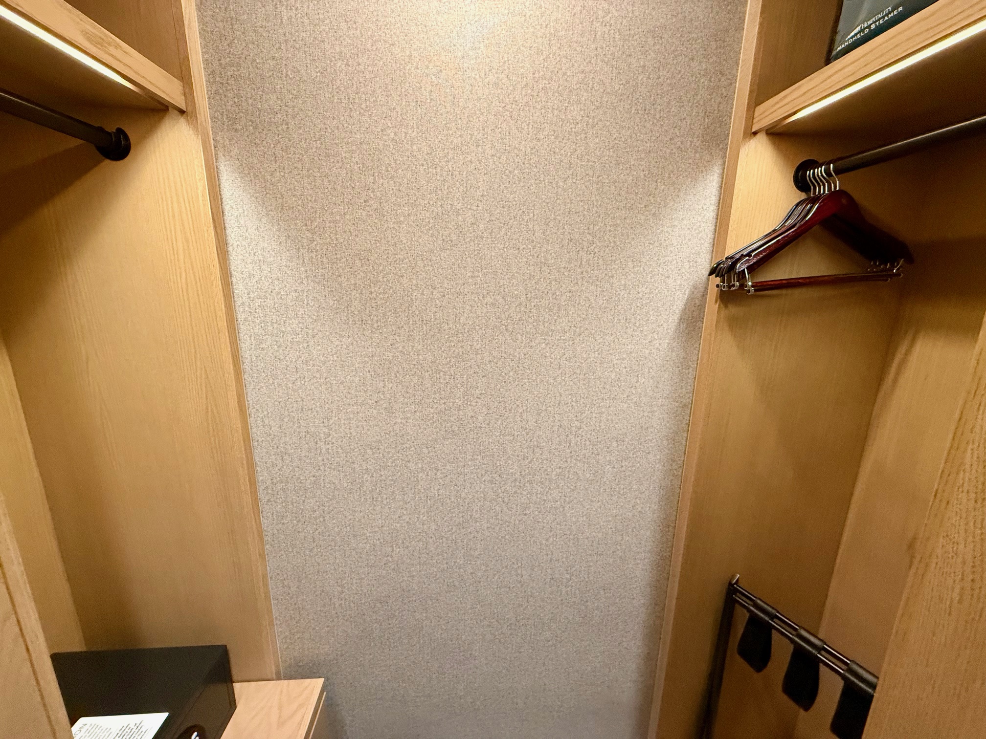a closet with a white wall and a shelf with clothes swingers
