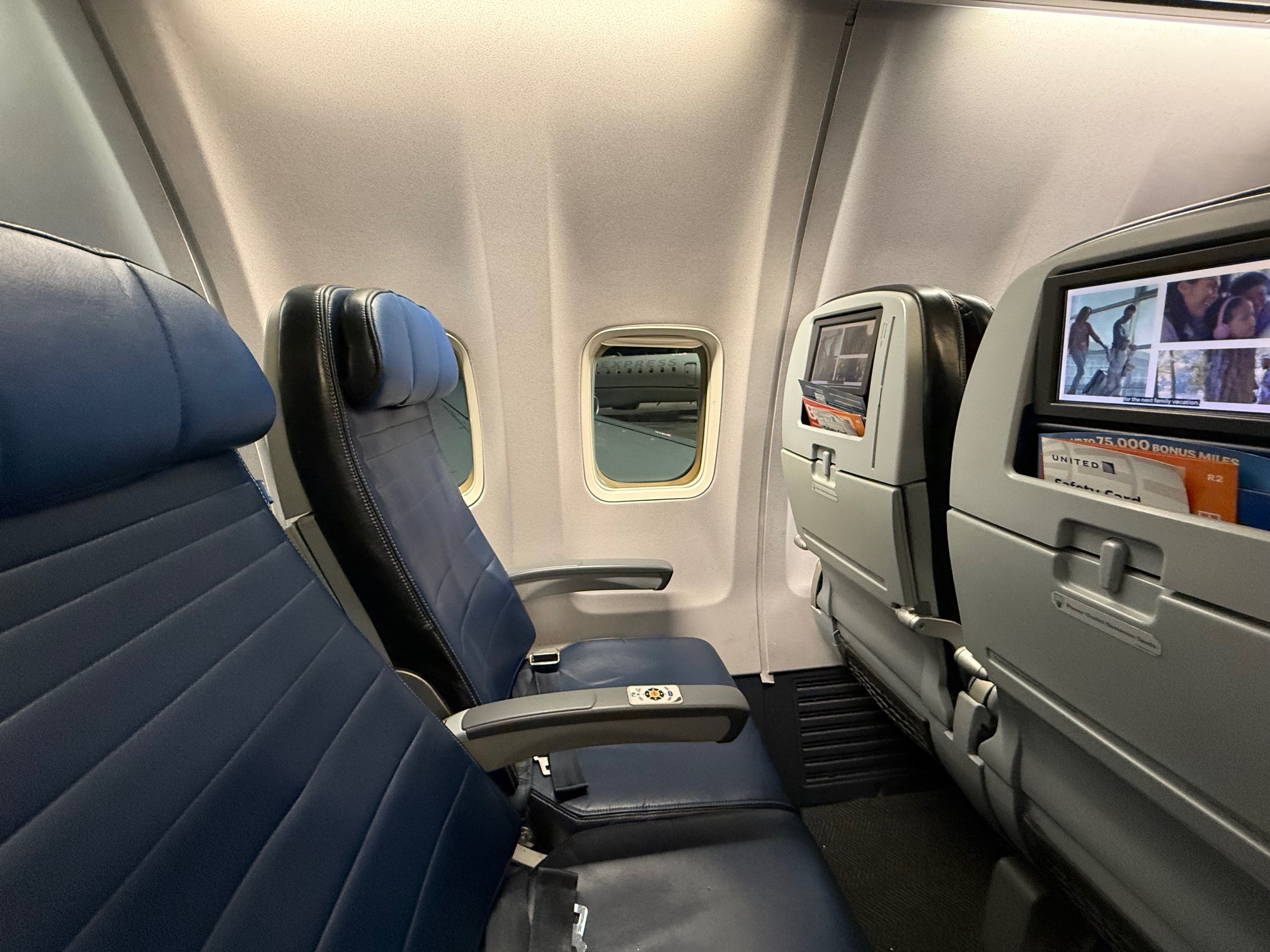 seats in an United 737-900ER airplane with a screen and a television