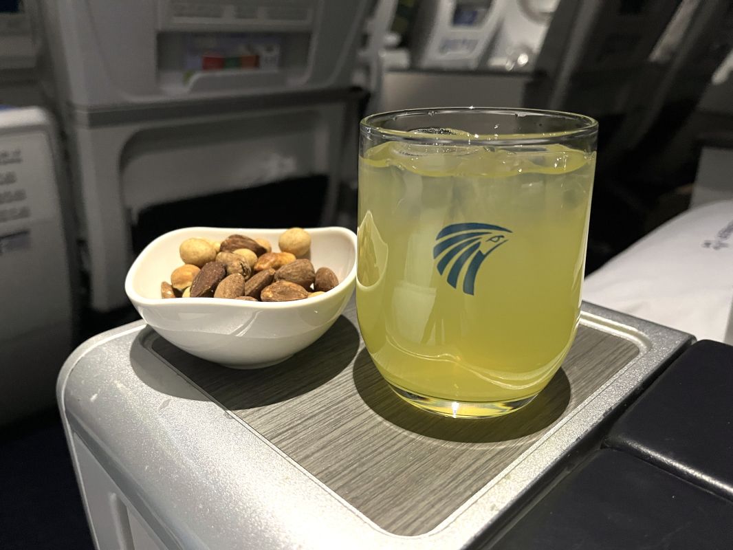 a glass of yellow liquid and a bowl of nuts on a tray