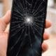 a hand holding a cell phone with a broken screen