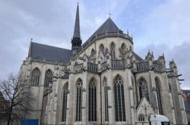 a large stone building with a steeple with Leuven in the background