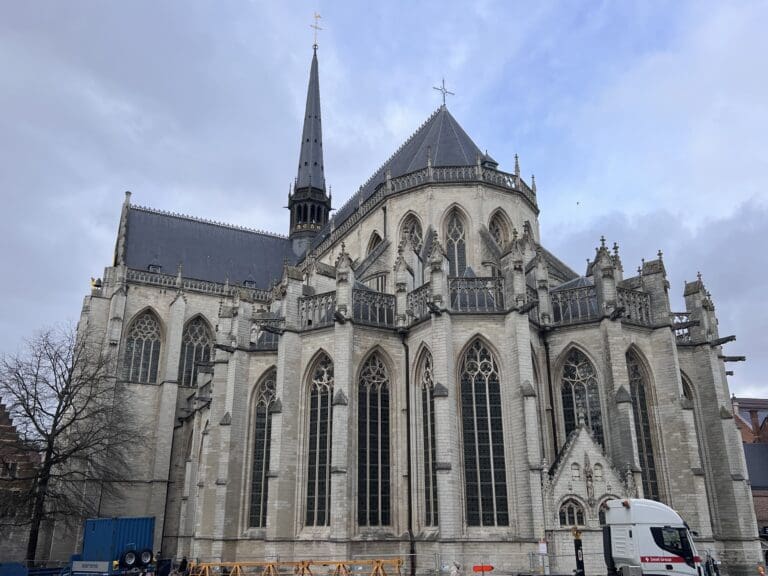 a large stone building with a steeple with Leuven in the background