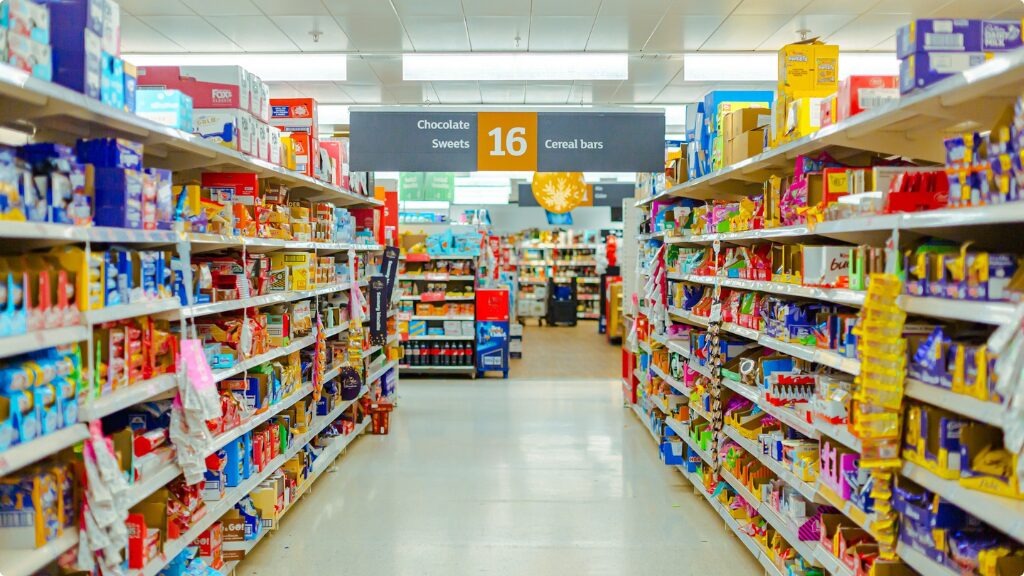 An aisle in a grocery store with products on shelves and a sign hanging above the aisle